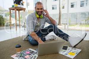 Smiling designer talking on mobile phone while using laptop