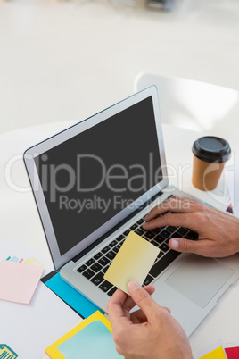Cropped hands of graphic designer holding adhesive note while using laptop