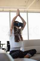 Young businesswoman doing yoga while using virtual reality on sofa