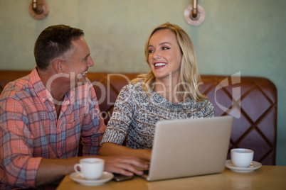 Couple interacting with each other while using laptop in restaurant