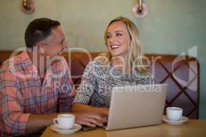 Couple interacting with each other while using laptop in restaurant