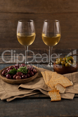 Black and green olives served in container by crackers with wineglass