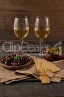 Black and green olives served in container by crackers with wineglass