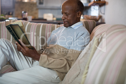 Senior man reading book while relaxing on sofa