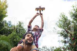 Low angle view of father carrying son playing with airplane