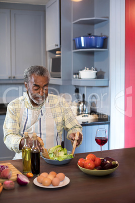 Senior man making salad while sitting in kitchen