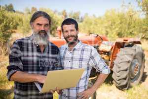 Portrait of happy friends using laptop in farm