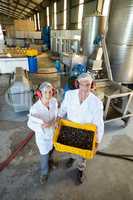 Portrait of happy technicians holding fresh olives in crate