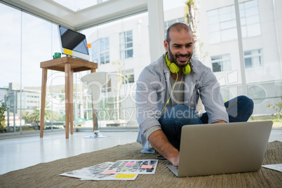 Smiling desginer using laptop while sitting on floor