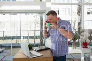 Designer having drink while talking on mobile phone