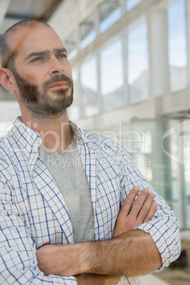 Thoughtful male designer with arms crossed seen through glass