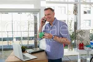 Portrait of smiling designer having drink while talking on mobile phone