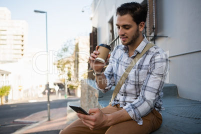 Smiling man having drink while using mobile phone