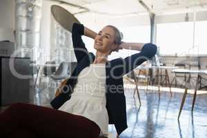Thoughtful businesswoman with hands behind head relaxing on chair