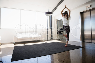 Full length of businesswoman wearing virtual reality simulator practicing tree pose