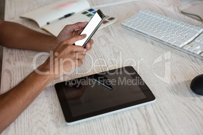 Cropped hands of man using phone over tablet in office