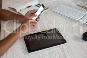 Cropped hands of man using phone over tablet in office