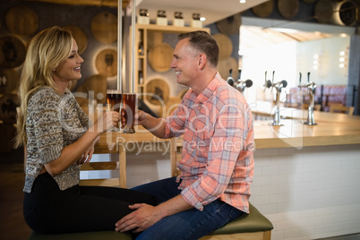 Couple interacting while toasting a glass of beer at bar counter