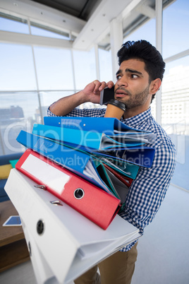 Male executive holding stack of files while talking on mobile phone