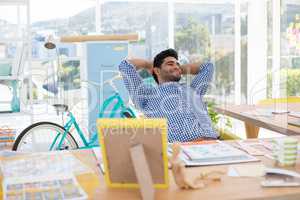 Male executive relaxing with hands behind head at desk