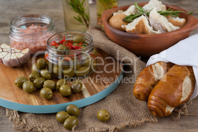 Green olives with containers on cutting board by bread