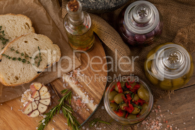 Olives in glass jars with ingredients and bread on table