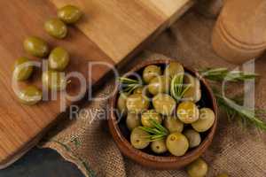 Olives with rosemary in bowl by cutting board