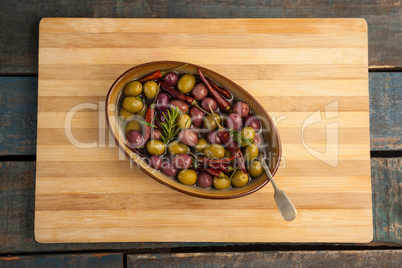 Olives with red chili pepper in container on cutting board