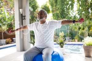 Senior man with arms outstretched lifting dumbbell while exercising
