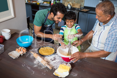 High angle view of father and grandfather looking at boy making food
