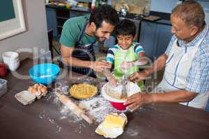 High angle view of father and grandfather looking at boy making food
