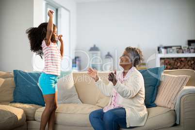 Grandmother applauding her granddaughter while dancing in living room