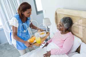 Female doctor serving breakfast to senior woman on bed