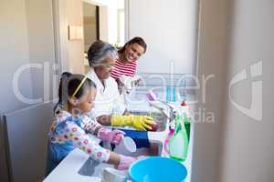 Grandmother and granddaughter washing utensil in kitchen sink