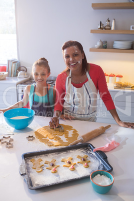 Smiling mother and daughter preparing cookies in kitchen worktop