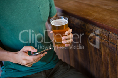 Midsection of man using phone while having beer