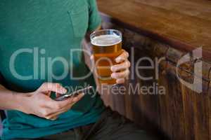 Midsection of man using phone while having beer