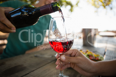 Man pouring wine in glass held by female friend