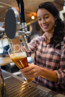 Pretty barmaid pouring beer from tap in glass