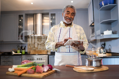 Portrait of smiling man using tablet computer while cooking food