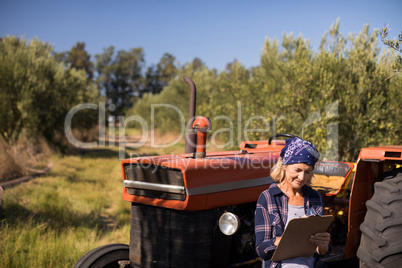 Woman leaning on tractor while writing on clipboard