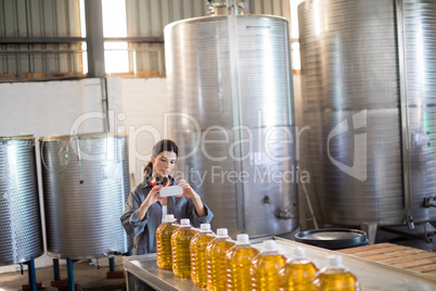 Female worker taking photo of oil bottles from mobile phone