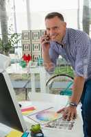 Portrait of smiling designer talking on mobile phone at desk in office
