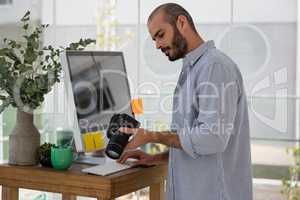 Designer examining camera while standing by computer