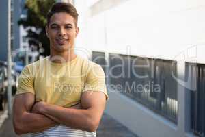 Portrait of handsome young man with arms crossed standing on sidewalk