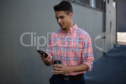 Young man using mobile phone while walking by wall