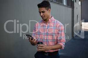Young man using mobile phone while walking by wall