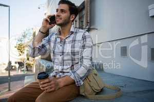 Man talking on mobile phone while sitting on retaining wall