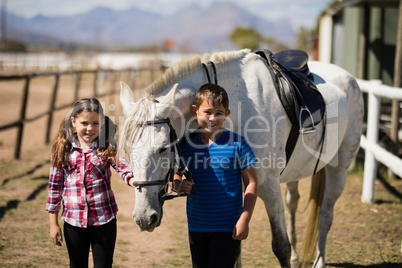 Siblings standing with white horse in the ranch