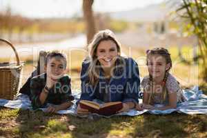 Smiling mother and kids reading novel in park